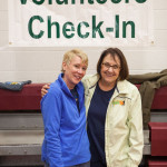 Two smiling women standing under Volunteer Check-In banner