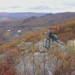 Small group of hikers perched on rocks at top of mountain looking out across Berkshire Mountain fall scenery